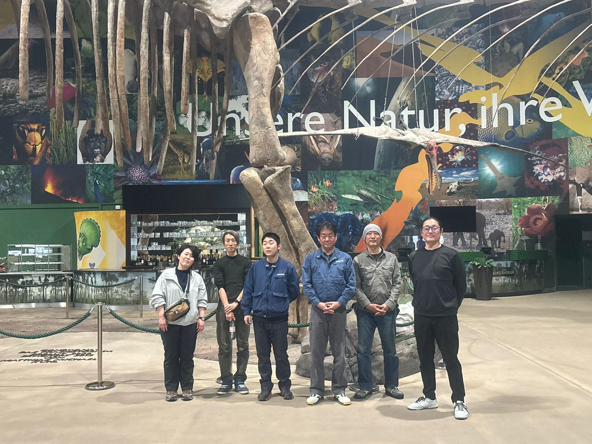 Das Team der japanischen Robotik-Spezialisten steht unter dem imposanten Argentinosaurus-Skelett.